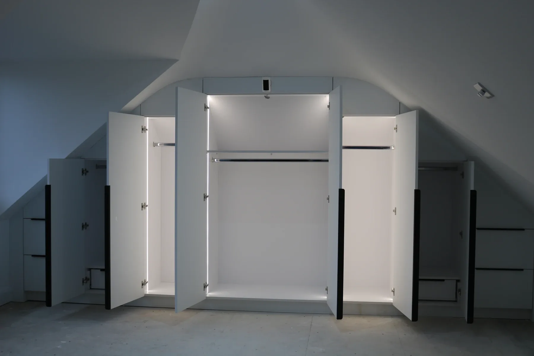 Fitted wardrobes scribed into a curved sloping loft ceiling with LED-lit interiors, doors open on handover day
